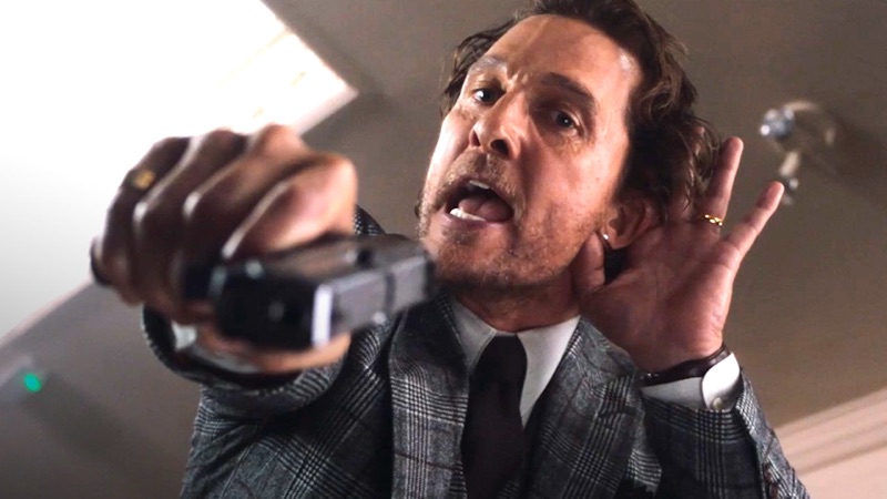 A still from Guy Ritchie's The Gentlemen showing a suited man drawing a gun